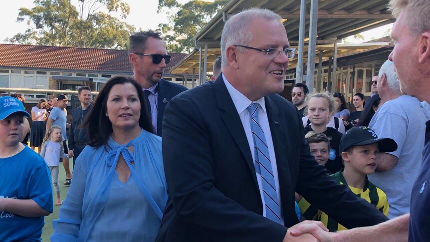 Scott Morrison shakes the hand of a constituent with his wife close behind him, and crowds milling around