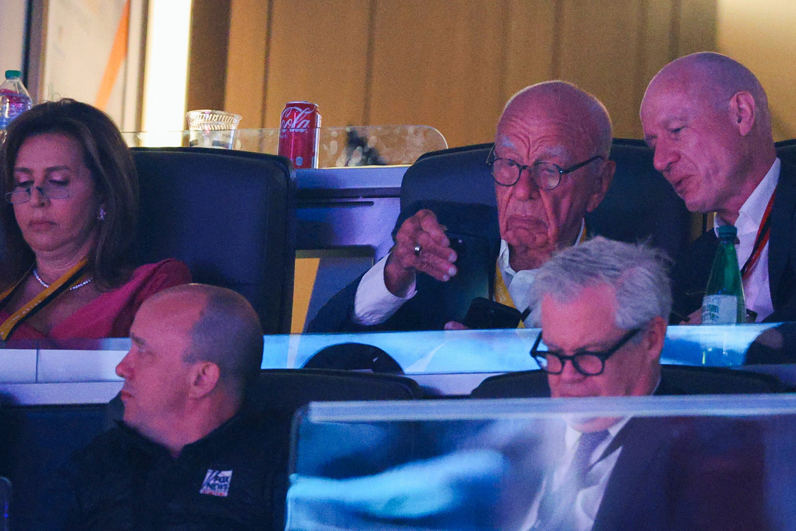 Rupert Murdoch, squinting at a phone screen, in a crowded auditorium 