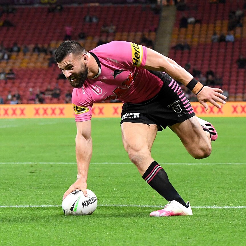 A Penrith NRL player grounds the ball across the line with his right hand to score a try against Brisbane.