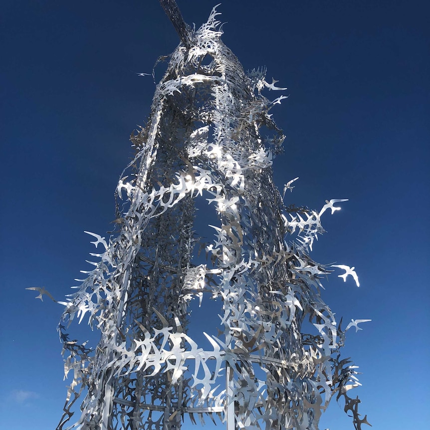 The tip of a metal sculpture constructed out of thousands of metal birds linked together.
