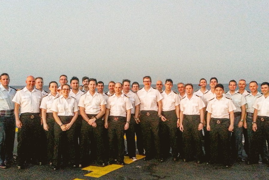 Naval officers in short-sleeved shirts on the deck of a ship.