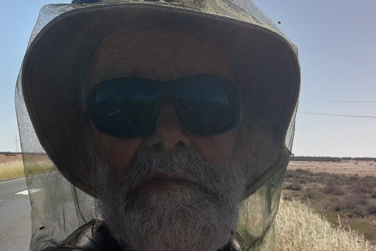 70-year-old man with white beard wearing fly net over face and dark sunglasses