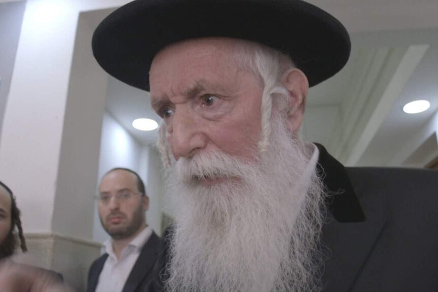 Image of a rabbi standing in a corridor outside a courtroom looking at someone