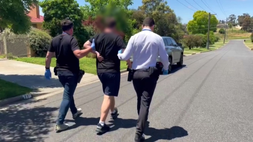 Two police officers taking a man to a car