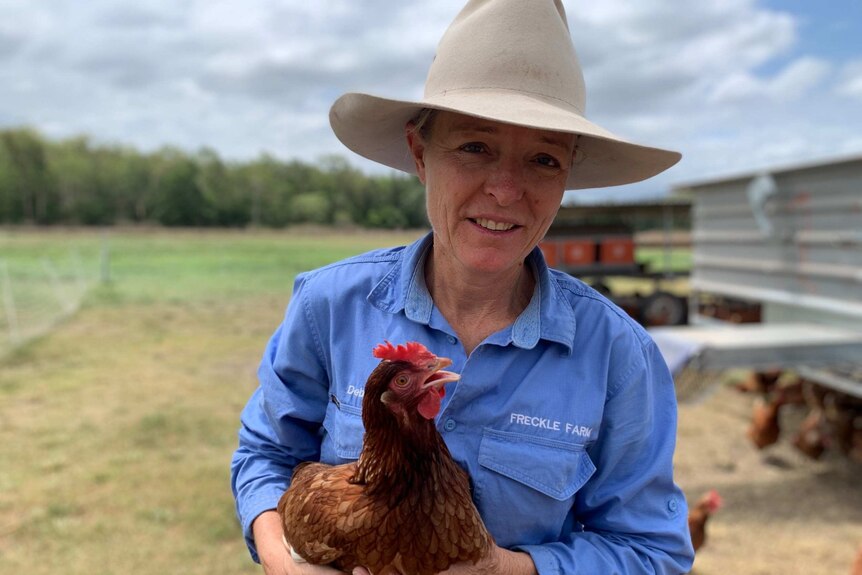 A middle-aged woman in a hat holding a hen