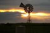 The sun sets behind a windmill on a rural property.