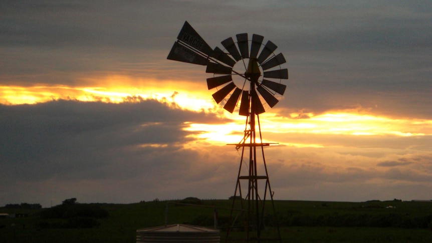 The sun sets behind a windmill on a rural property.