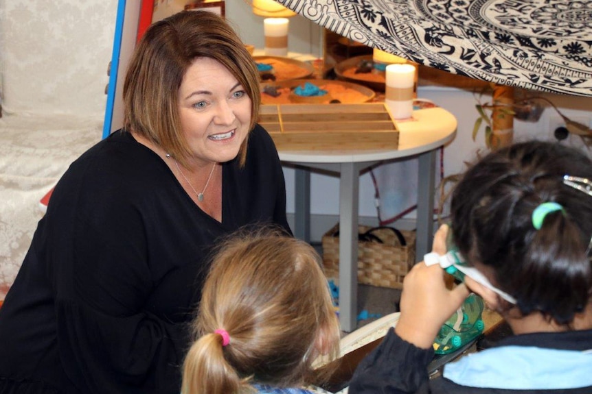 School principal Rebecca Burns sits on the the classroom floor with students.