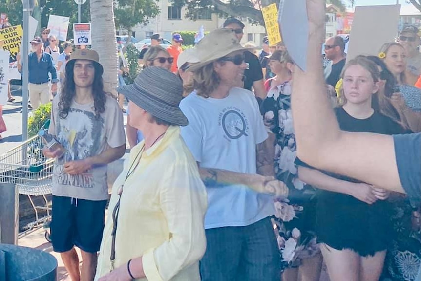 A man surrounded by other people wears a tshirt with the letter Q on it. 