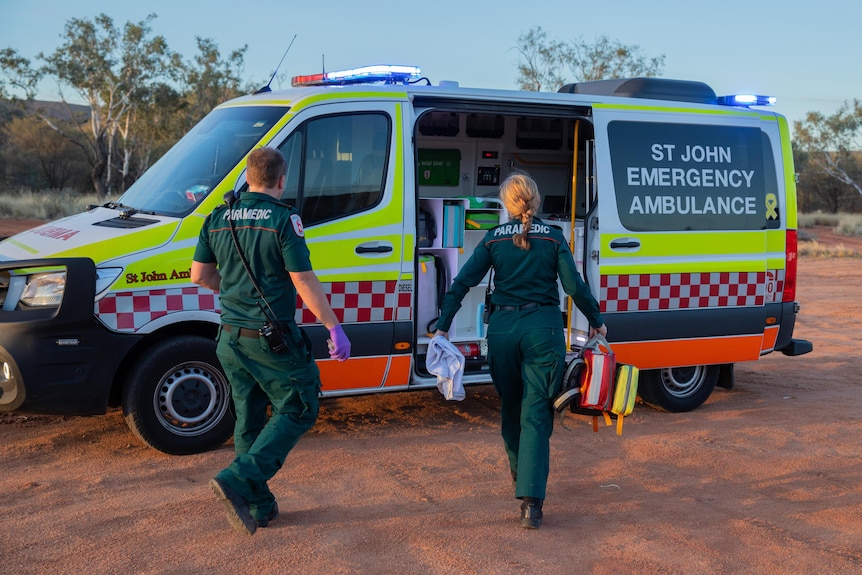 Two paramedics walk towards an ambulance which has an open sliding door.