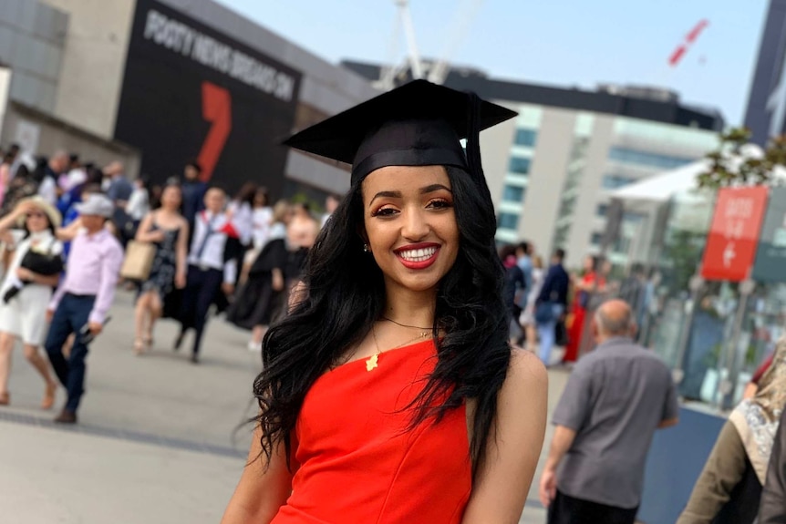 A young woman poses for a graduation photo in front of crowds