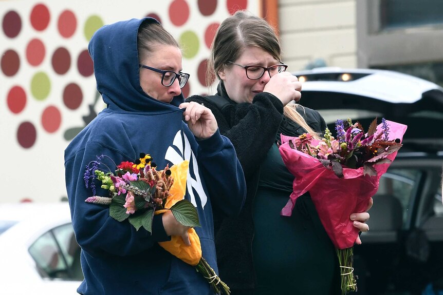 Two women holding flowers and crying