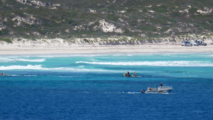 Boats in the water conducting a search near the shore of a beach.