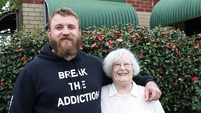 Man with beard wearing a 'hoodie' with the words BREAK THE ADDICTION  with his arm around his grandmother