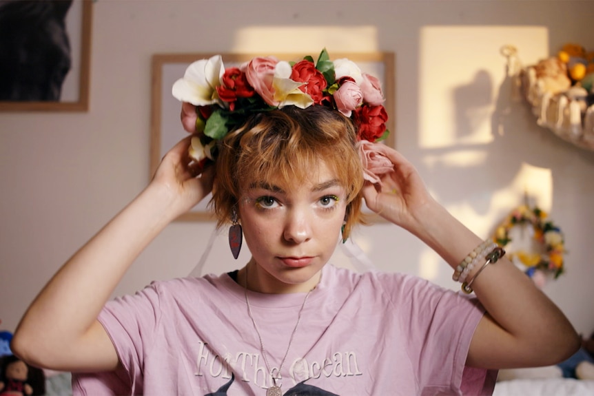 A young woman places a flower crown on her head. 