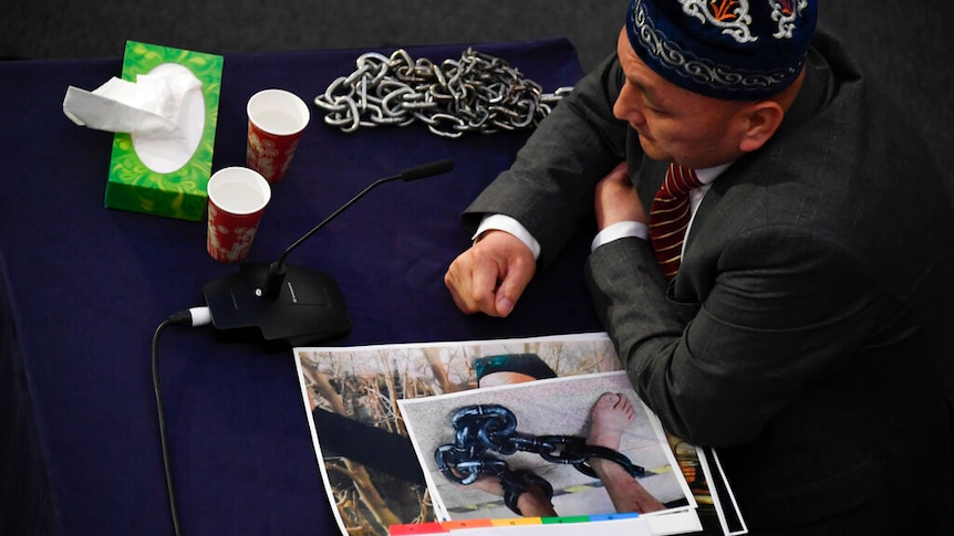 Omir Bekali gives evidence with a photo of shackled feet by his hands.