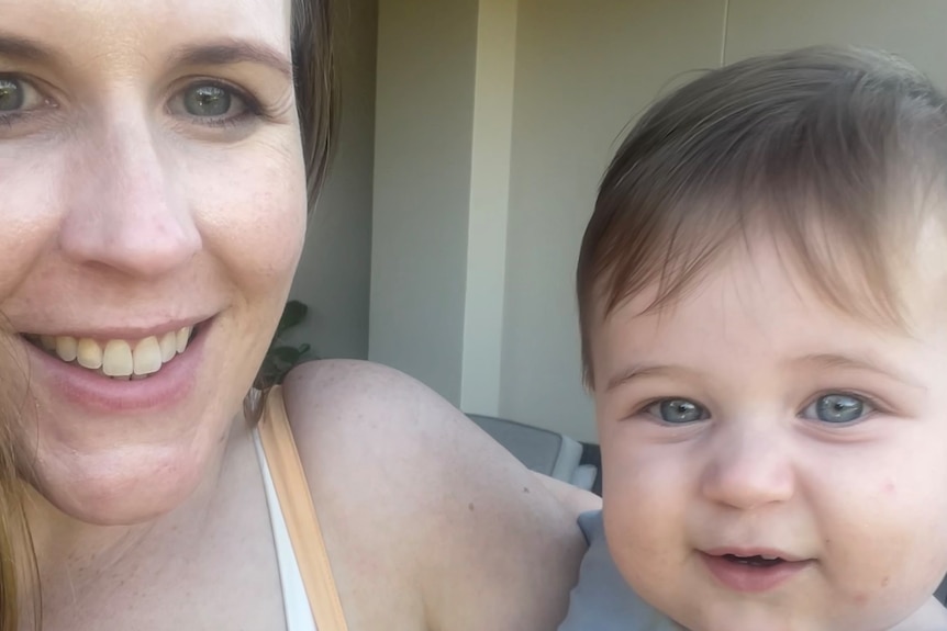 a woman smiling, holding a young baby boy