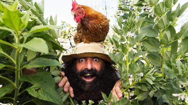 a photo of a man with a large black beard smiling with a chicken on his head