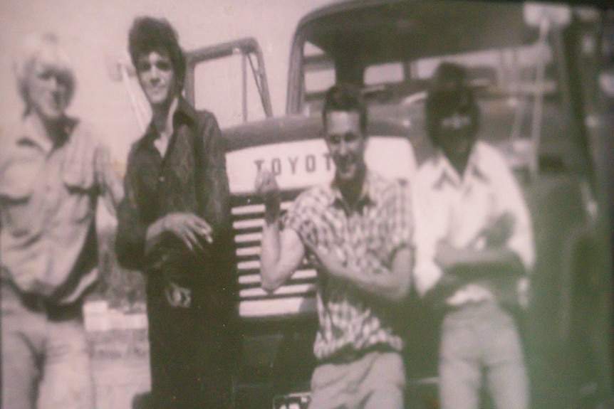 A black and while photo of four men next to a bus.