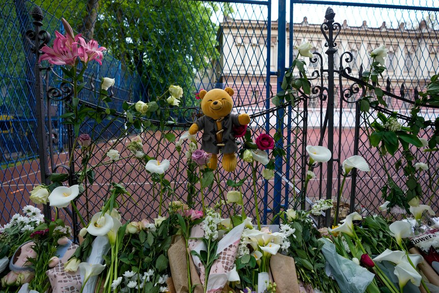 A teddy bear can be seen pinned to a gate among flowers in a shrine for victims for a shooting in Belgrade