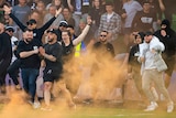 A group of people run onto a pitch, with orange haze from flares around them.