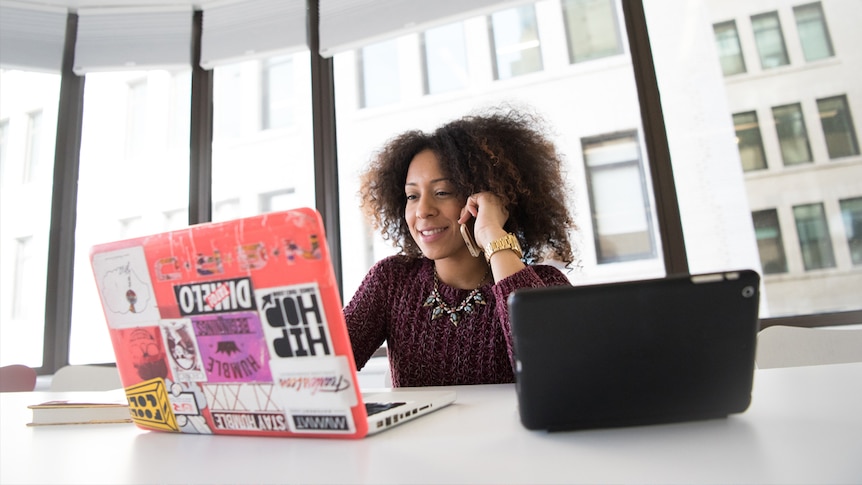 Woman sitting looking at her laptop while on the phone trying to find part-time work