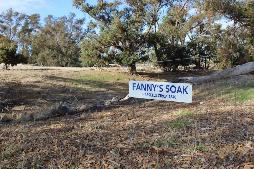 A dried up water hole with a fence and sign on the fence.