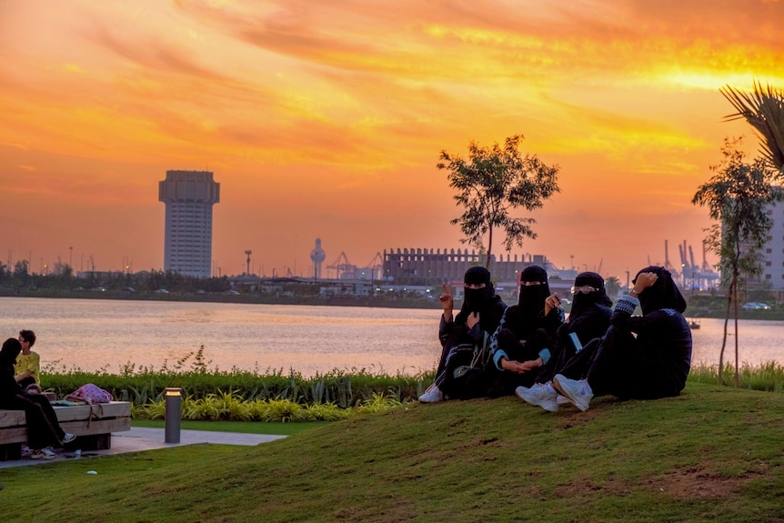 Four girls wearing black face coverings sit but a lake.