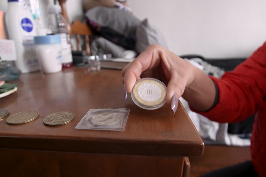 Woman holding up a sobriety coin on top of a cabinet.