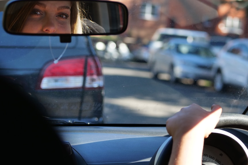 Domestic violence survivor Rachael* looks in the rearview mirror of her car.