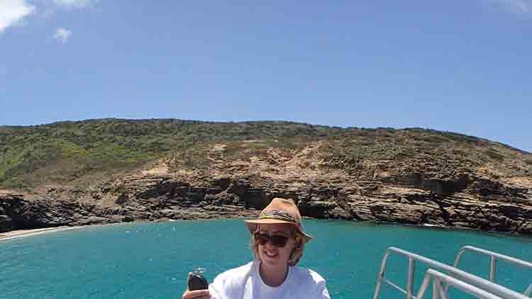 A woman stands on a boat holding up a bag of rubbish as its weighed.