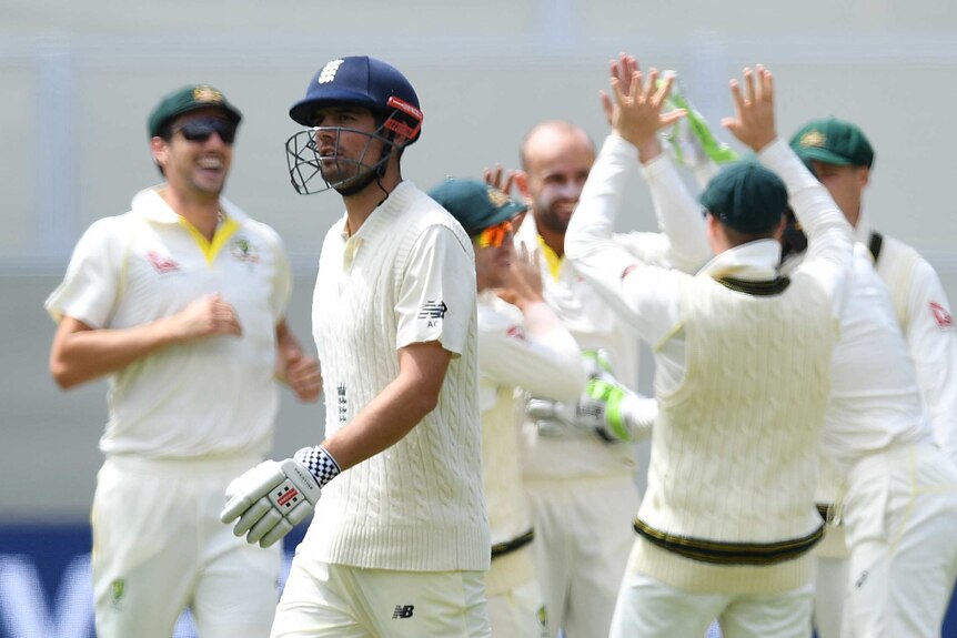 Alastair Cook leaving the field as Australian players celebrate in the background.