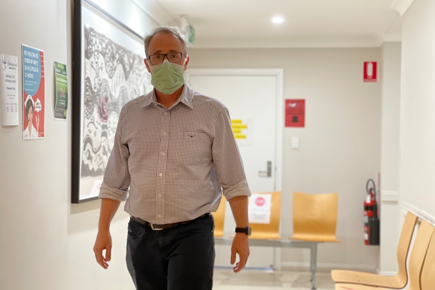 A man wears a mask and walks down the hallway of his practice. 