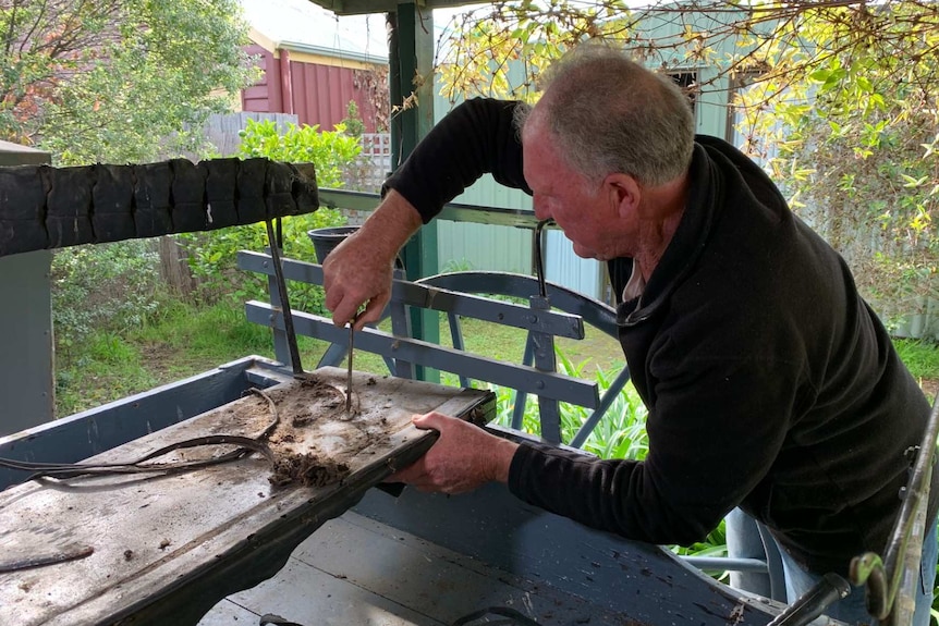 Rick Anderson uses a screw driver to scrape debris off an old horse-drawn carriage he is restoring