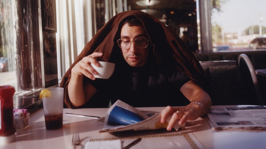 Bleachers' Jack Antonoff reads the paper and has a cup of coffee with a jacket over his head