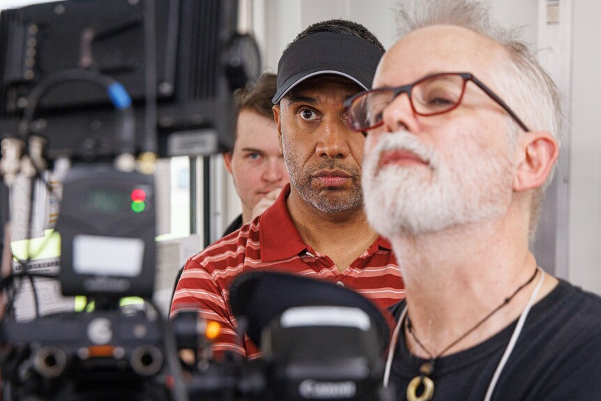three men looking at a camera on a film shoot