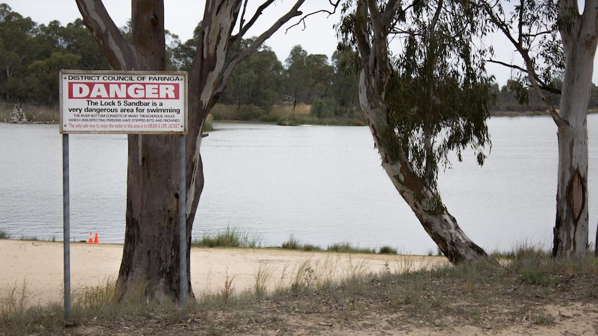 A warning sign on the foreshore of a body of water.