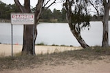 A warning sign on the foreshore of a body of water.