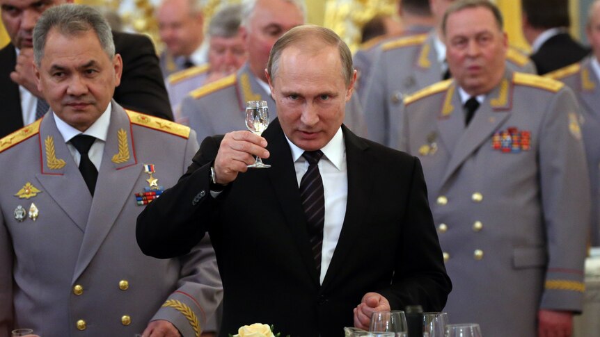 Vladimir Putin raises a champagne glass looking serious