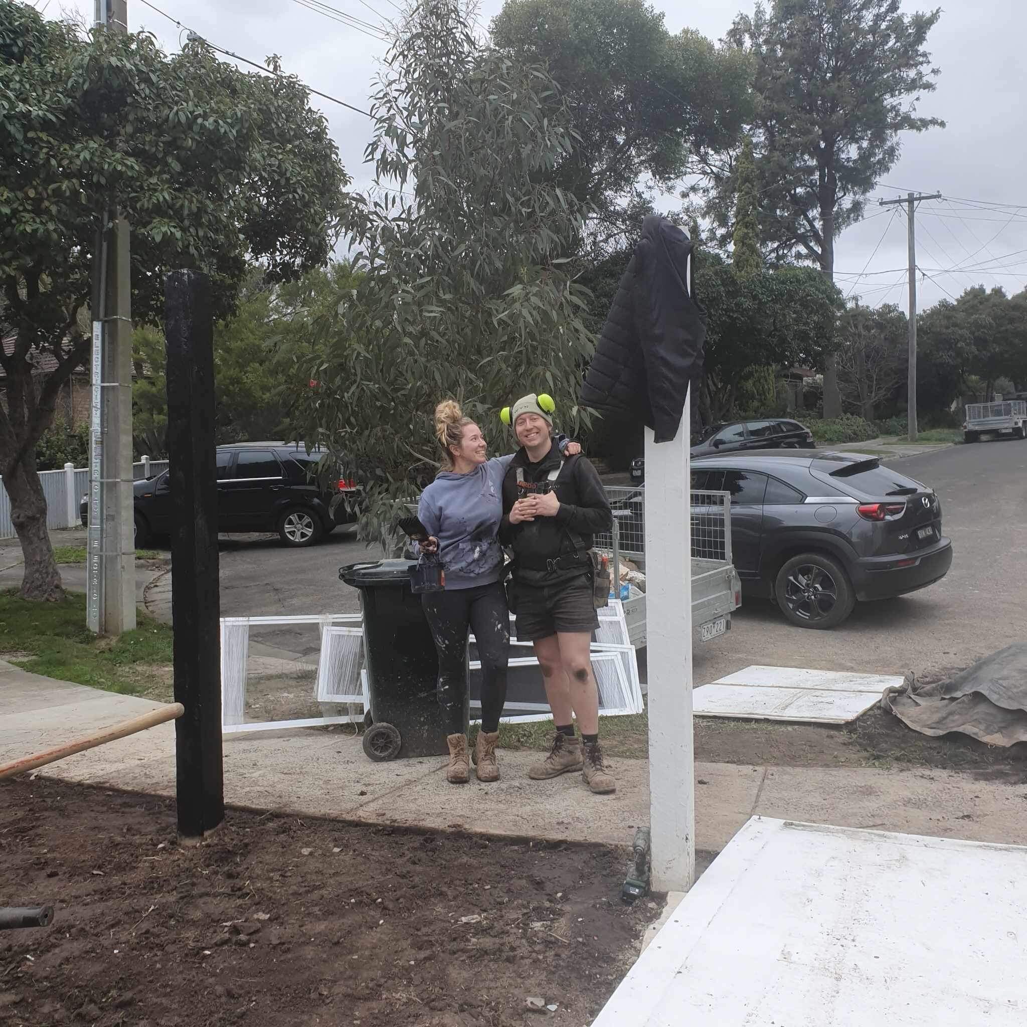 A young couple wearing dirty work clothes stand together at the front of a block under construction