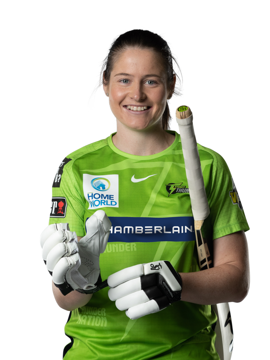 Young woman holding a cricket bat under her arm putting on her batting gloves and smiling