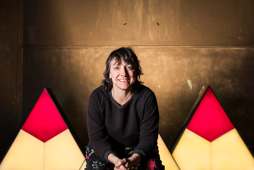 Colour photo of Powerhouse Youth Theatre Fairfield Artistic Director Karen Therese sitting in front of props inside a theatre.