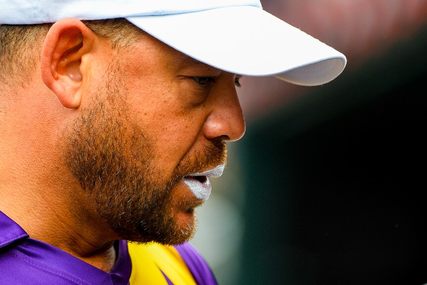 Andrew Symonds looks downwards while wearing a white cap