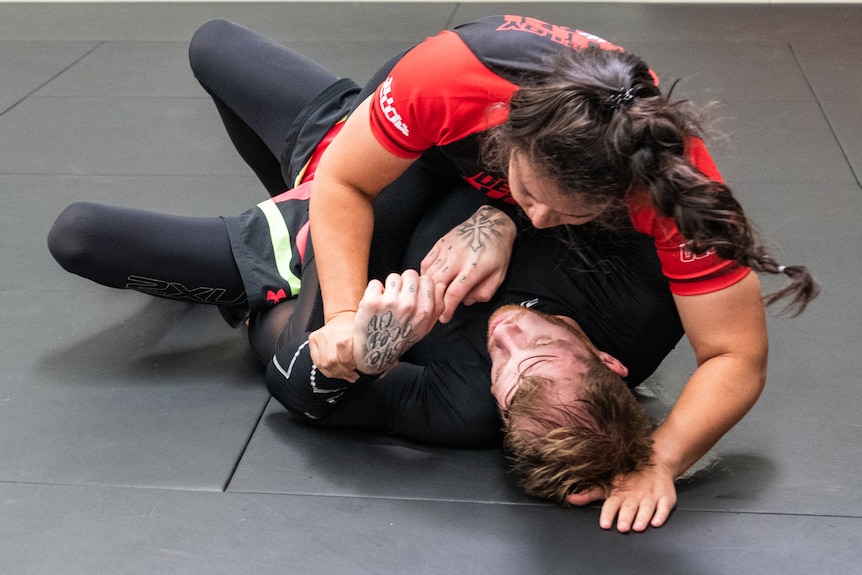 A woman grapples with a man on a gym mat.