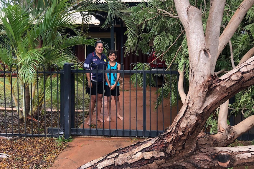 A woman and her young son in the driveway of their house which is blocked by a fallen tree.