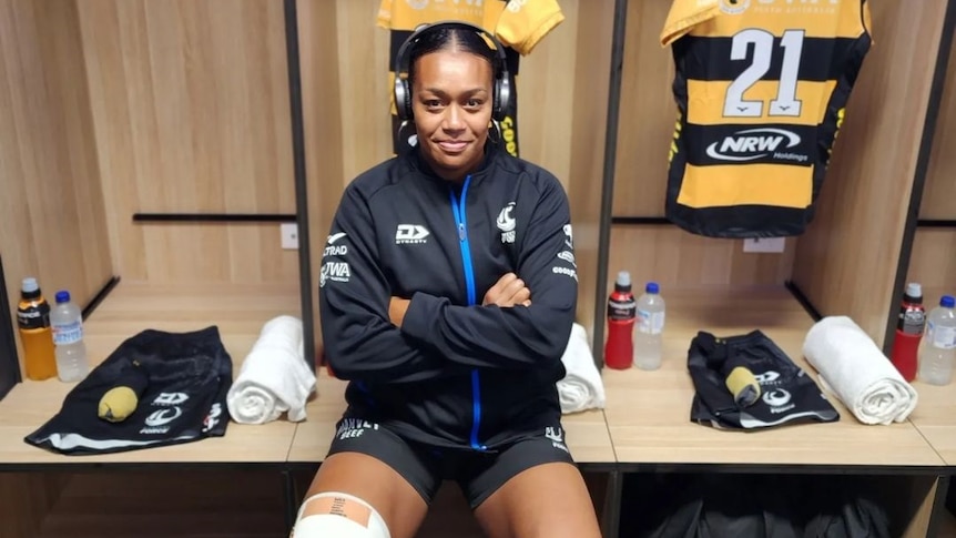 Sera Ravatudei sits in the change room, wearing headphones with her jersey on a hanger behind her.