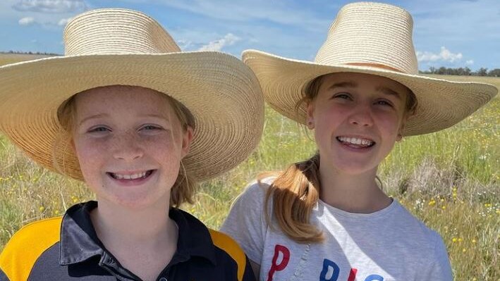 Two girls in akubras hold a tub of picked yellow wildflowers