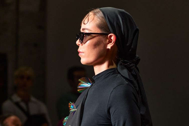 A woman wearing a black outfit and headscarf and sunglasses.