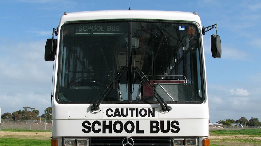A white school bus parked on an oval. It reads 'Caution School Bus' in black letters