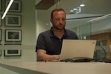 A man sits looking at his laptop